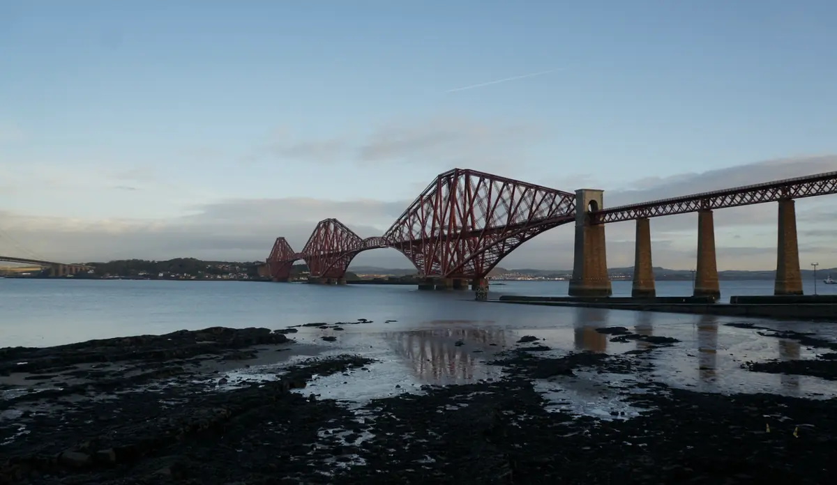 Il Forth Bridge visto da South Queensferry al crepuscolo, riflesso sulla battigia